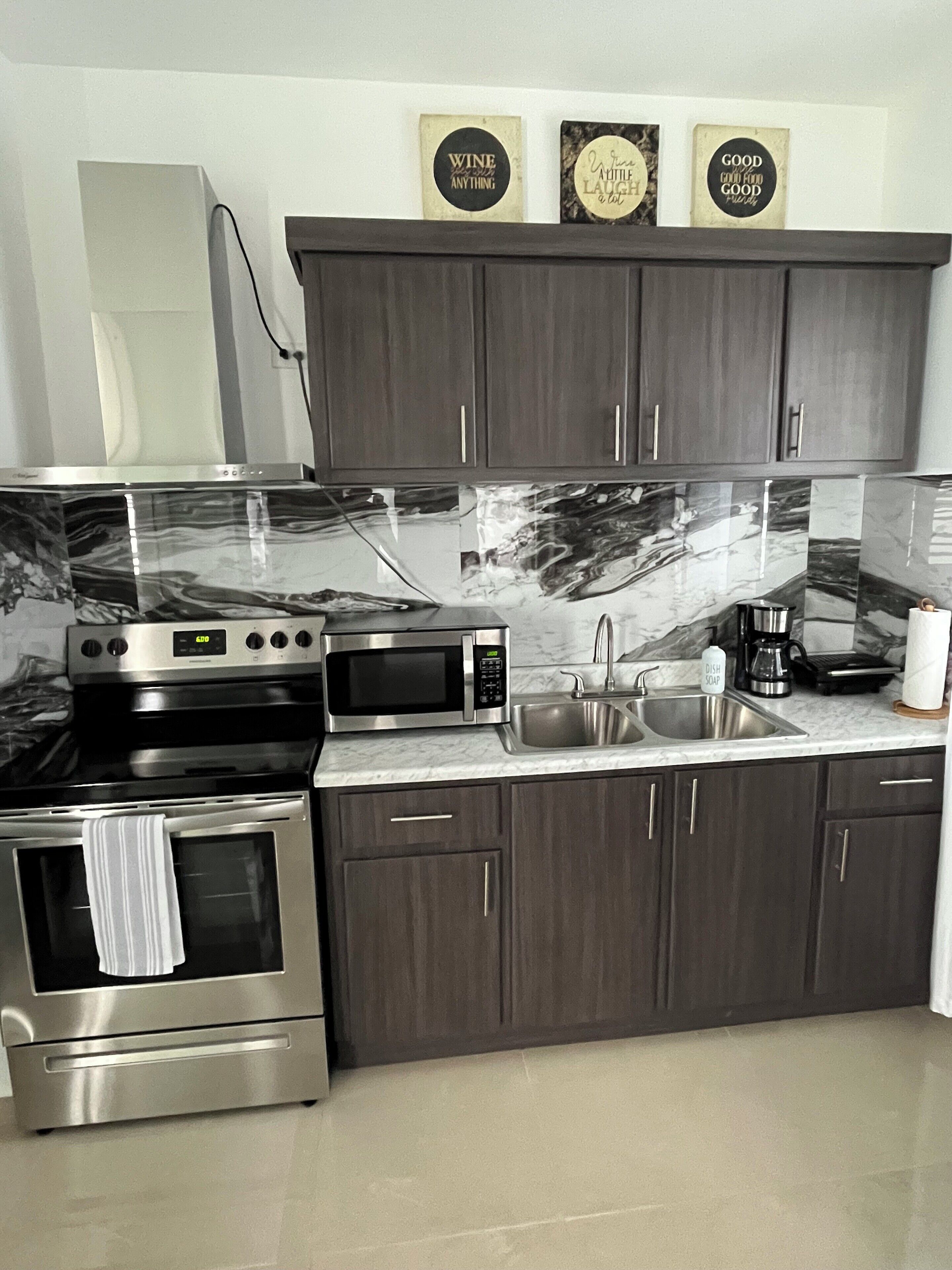 A modern kitchen with dark wooden cabinets, stainless steel appliances including a microwave, oven, and coffee maker, and a marble backsplash.