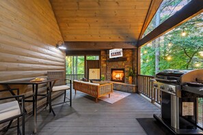 A cozy cabin interior with a stone fireplace, wooden deck, and outdoor grilling area.