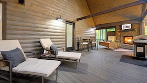 A wooden deck with lounge chairs and a stone fireplace. - Cozy Nights Await at Ember & Stone– 3 Fireplaces, Hot Tub & Tucked Away Vibes (Broken Bow)