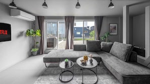 A modern living room with a grey sectional sofa, two round coffee tables, and a flat-screen TV mounted on the wall. - SNOWGARDEN YIG STAY (Furano)