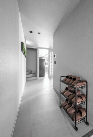 Un couloir avec un porte-chaussures en métal, un escalier et une porte donnant sur une autre pièce.
