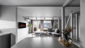 A modern living room with a large grey table, a sofa, and a TV mounted on the wall. - SNOWGARDEN YIG STAY (Furano)