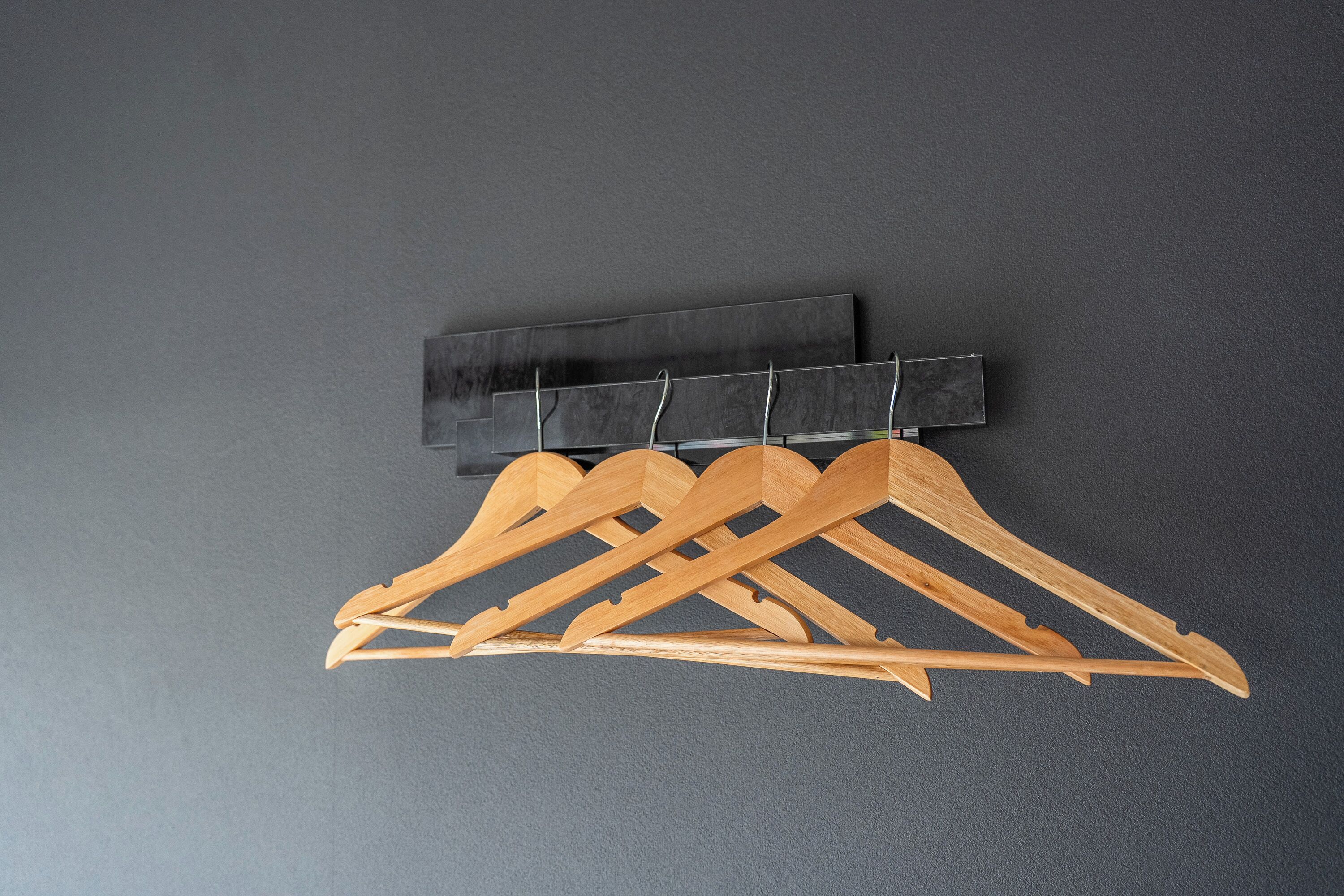 Eine wandmontierte Garderobenstange aus Holz mit mehreren Kleiderbügeln an einer grauen Wand.