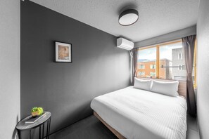 A modern hotel room with a large bed, a small side table with a plant, a framed picture on the wall, and a window with curtains. - WHITEGARDEN YIG STAY (Furano)