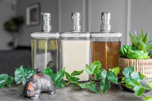 Three clear glass bottles labeled body soap, conditioner, and shampoo on a countertop with green plants and a small turtle figurine. - WHITEGARDEN YIG STAY (Furano)