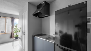 A modern kitchen with a stainless steel refrigerator, a built-in oven, and a window with a view of the city. - WHITEGARDEN YIG STAY (Furano)