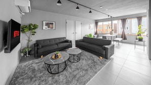 A modern living room with a grey sofa set, two round coffee tables, and a flat-screen TV displaying Netflix. - WHITEGARDEN YIG STAY (Furano)