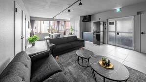 A modern hotel room with a sofa, a round table, and a kitchen area. - WHITEGARDEN YIG STAY (Furano)