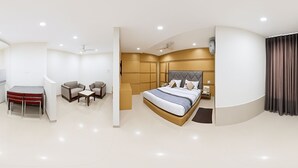 A modern hotel room with a large bed, a desk, two chairs, and a small table.