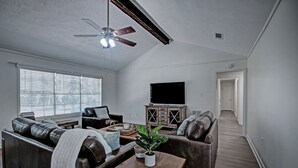 A spacious living room with a ceiling fan, a flat-screen TV, and a wooden cabinet. - The Rez Retreat - King Beds (Brandon)