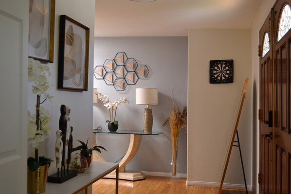 Une pièce avec une table en verre, une lampe, un vase contenant des plantes séchées et un jeu de fléchettes accroché au mur.