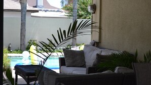 Ein Poolbereich mit weißem Sofa, Korbsessel und einer großen Pflanze.
