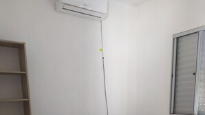 A bedroom with a bed, a wardrobe, a shelf unit, and an air conditioning unit.