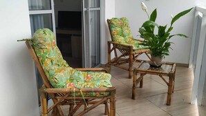 Two bamboo chairs with floral upholstery, a potted plant, and a sliding glass door in a room with tiled flooring.