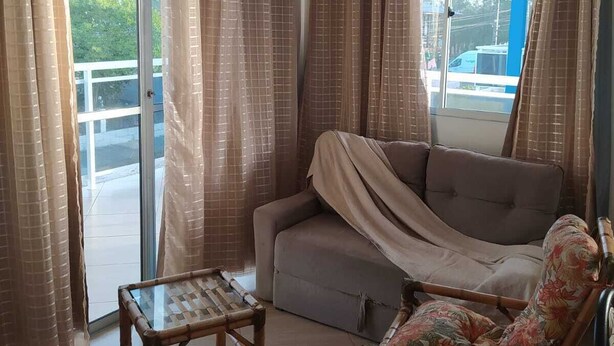 A living room with a sofa, a chair, and a small table. There is a sliding glass door with curtains.