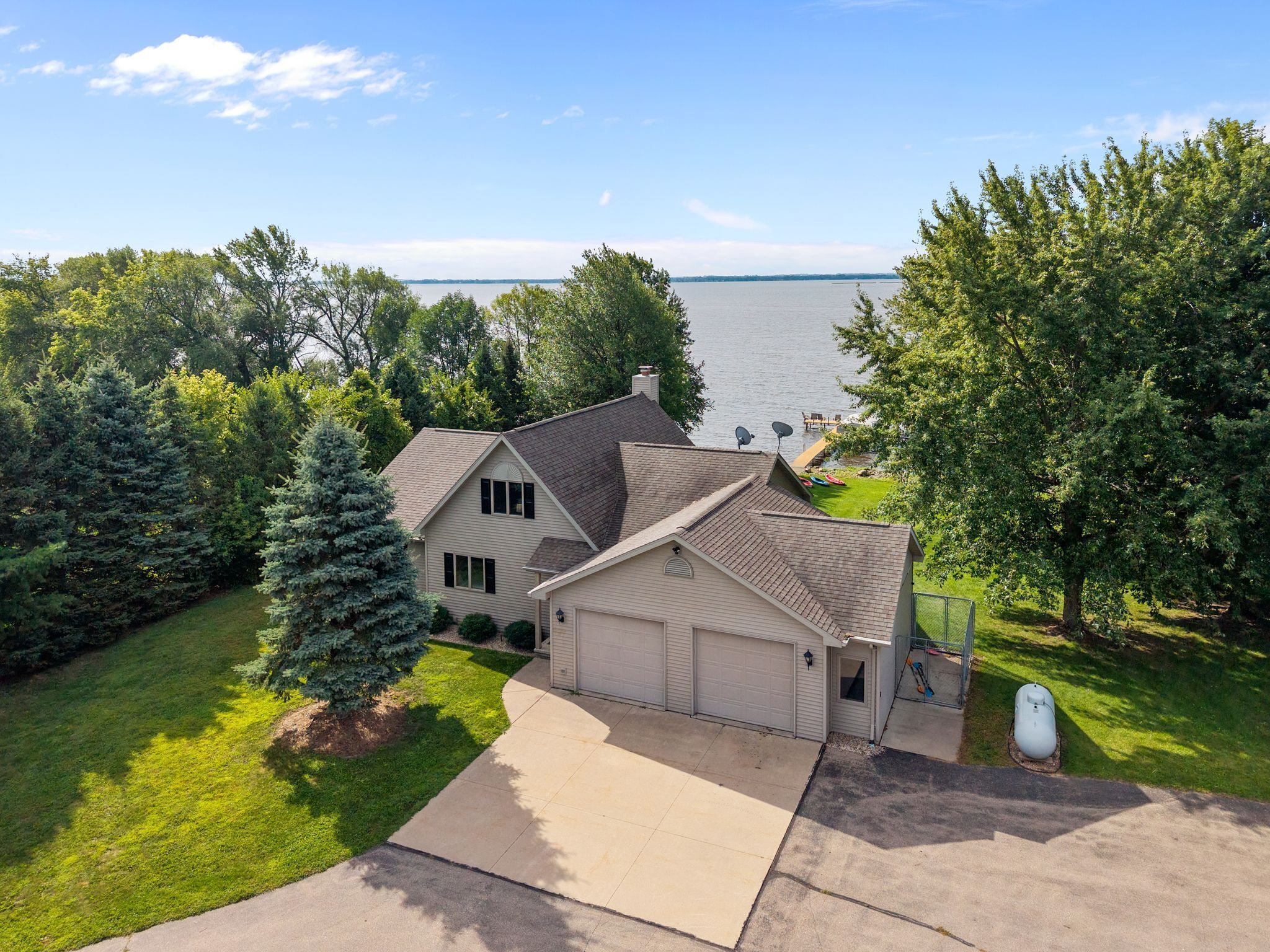 A two-story house with a garage, surrounded by trees and a view of a lake.