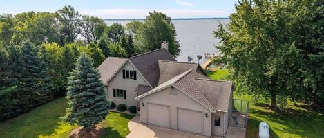 A two-story house with a garage, surrounded by trees and a view of a lake.