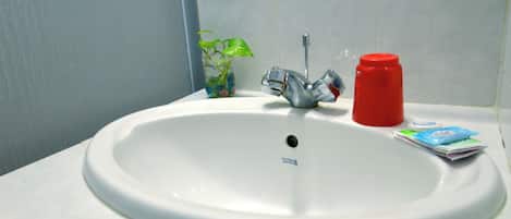 A white bathroom sink with a faucet, a red bottle, and a small plant in a glass container.