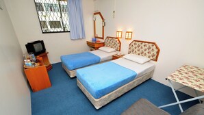 Habitació petita i senzilla amb dos llits, una taula petita, una televisió i una finestra amb cortines.