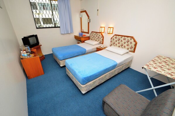 A small, simple room with two beds, a small table, a TV, and a window with curtains. - Hotel Lutana (Sandakan)