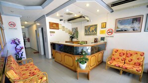 Zona de recepció d'hotel amb un taulell d'informació, dos sofàs, una planta en test i diversos objectes emmarcats a les parets.