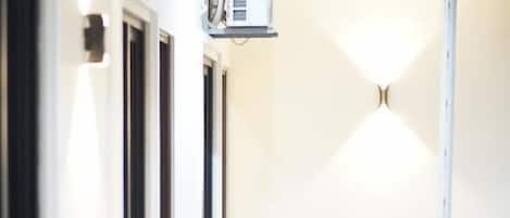 A corridor with air conditioning units, a tiled floor, and a wall-mounted light fixture.