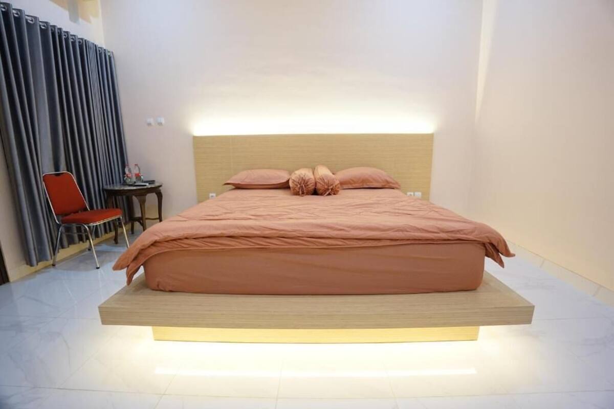 A modern bedroom with a large bed, a nightstand, a chair, and a curtain.