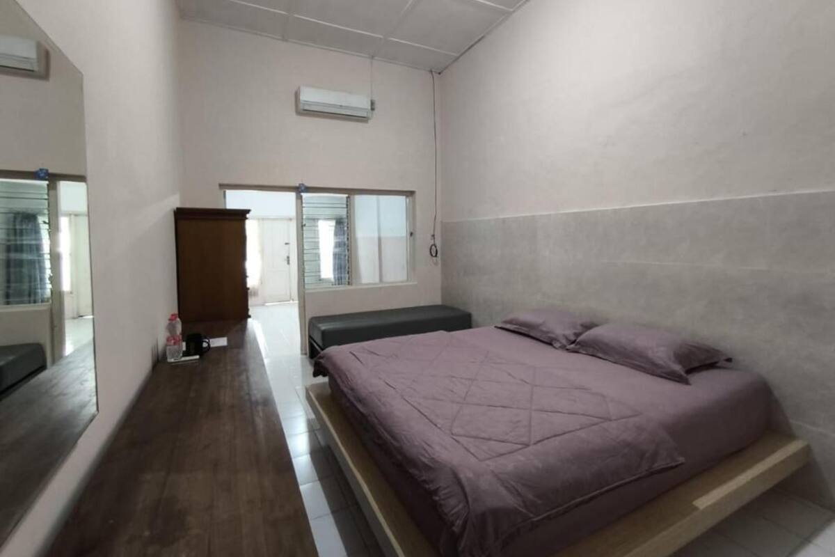 A bedroom with a bed, a wooden bench, a mirror, and a window.