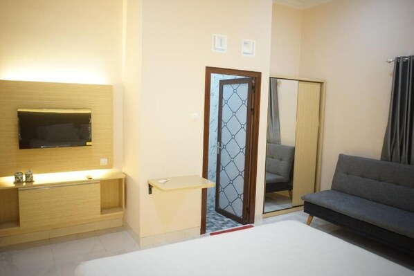 A hotel room with a bed, a TV mounted on the wall, a sofa, and a mirror. - House of Toti (Yogyakarta)