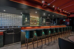 Un espace bar comprenant un comptoir, des tabourets de bar et une étagère où sont rangées les bouteilles.
