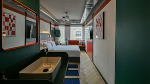 A modern hotel room with a large bed, a built-in sink, a small seating area, and a view of the city. - Nomas Hotel (Toronto)