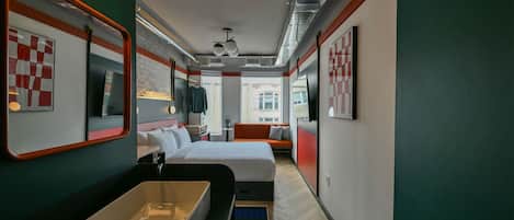 Habitación de hotel moderna con una cama grande, un lavamanos integrado, un pequeño rincón de estar y vistas a la ciudad.