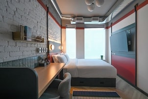 Habitación de hotel pequeña con pared de ladrillo, cama, escritorio con silla, televisor y ventana con vistas.