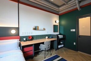 Een moderne hotelkamer met een bed, bureau, stoel en een kleine kitchenette.