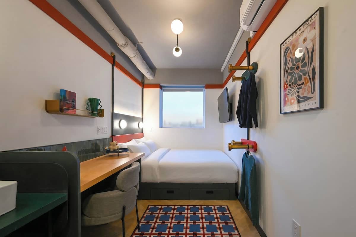 A compact hotel room with a bed, desk, chair, and a small window.