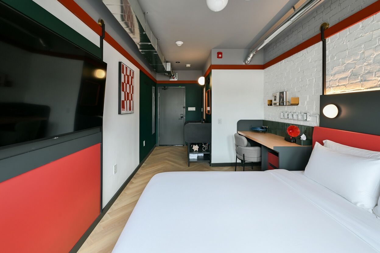 A hotel room with a bed, desk, chair, and a small kitchenette.