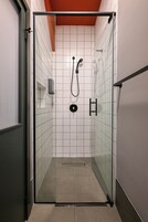 Douchecabine met glazen wanden, witte betegelde wanden, een zichtbare douchekop en een bedieningspaneel.
