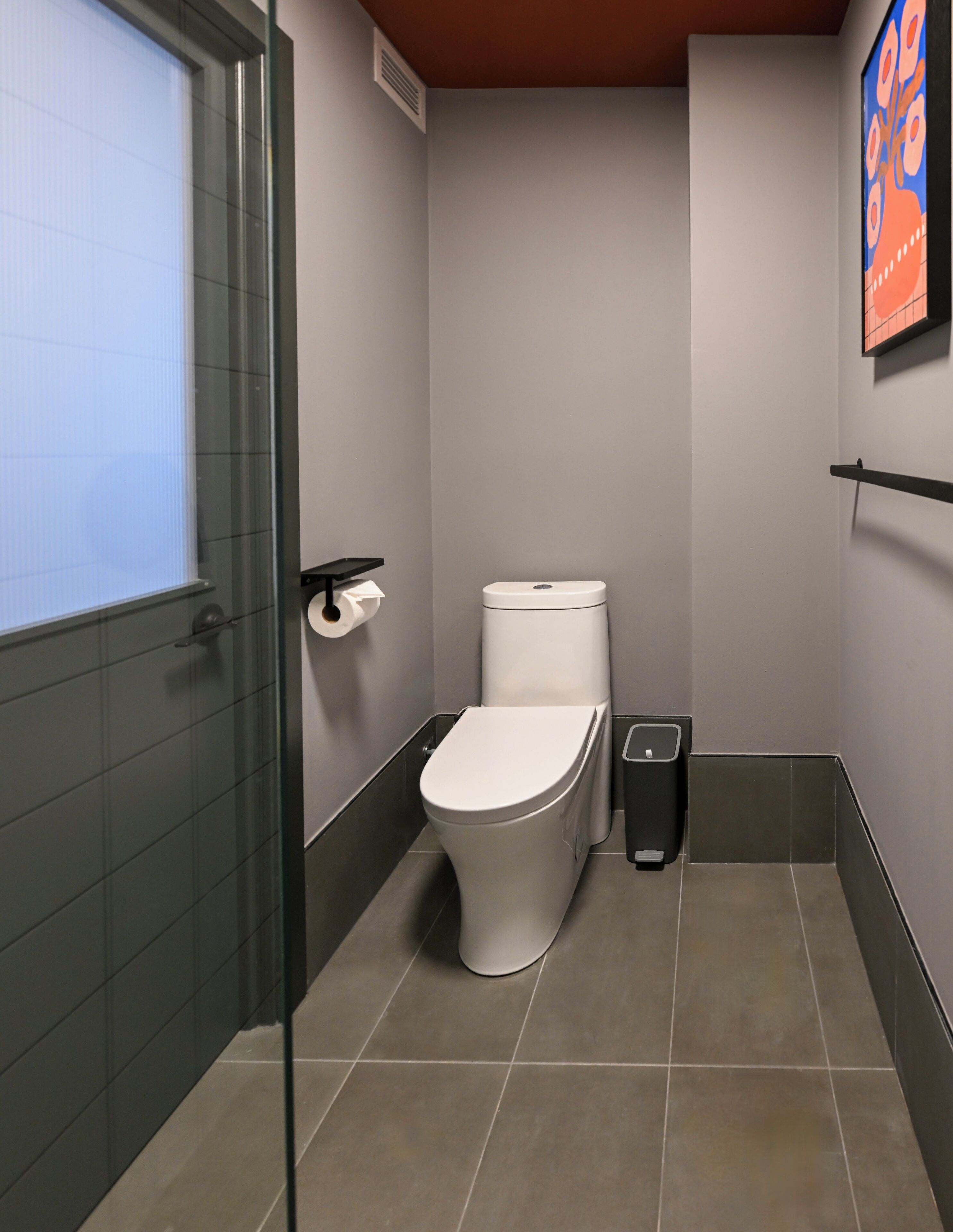 Ein Badezimmer mit Toilette, Mülleimer, Handtrockner und einer Glastrennwand.