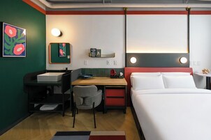 Habitación de hotel con cama, escritorio, silla y estante en la pared con libros.