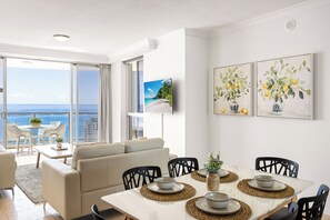 Et moderne spiseområde med havudsigt, en sofa og et bord dækket med tallerkener og en vase med blomster.