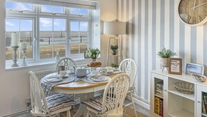 A dining area with a view of the beach, a large clock on the wall, and striped wallpaper.