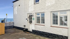 A white building with a stone facade, a door with a flower wreath, and a view of the sea.