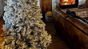 A cozy living room with a large Christmas tree, a fireplace, and a leather sofa.