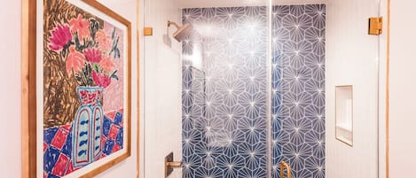 Un baño moderno con un estampado geométrico de azulejos, cabina de ducha de vidrio y una obra de arte enmarcada en la pared.