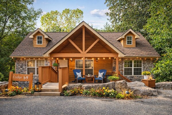 Un chalet avec une façade en pierre, un porche en bois et deux chaises Adirondack bleues.