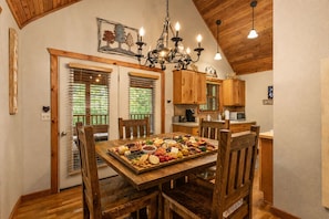 Un coin repas chaleureux, avec une table en bois dressée pour le repas, entourée de chaises en bois. Un lustre est suspendu au plafond, et la pièce est dotée de plafonds et de meubles en bois.