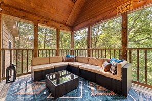 A covered porch with a sectional sofa, a glass-top coffee table, and a rug. - 2BR Creekside Cabin | Near SDC | Resort Amenities (Branson West)