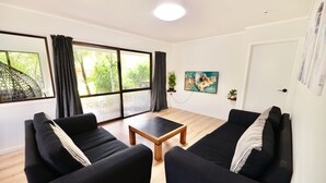 A living room with two black sofas, a wooden coffee table, and a large window with curtains. - Tamarillo Bach - Your Relaxing Beach Escape in Coopers Beach (Coopers Beach)