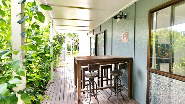 A wooden deck with a table and chairs, surrounded by greenery. - Tamarillo Bach - Your Relaxing Beach Escape in Coopers Beach (Coopers Beach)
