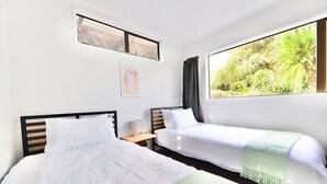 A hotel room with two beds, a small bedside table with a lamp, a window with a view of greenery, and a wall-mounted picture. - Tamarillo Bach - Your Relaxing Beach Escape in Coopers Beach (Coopers Beach)